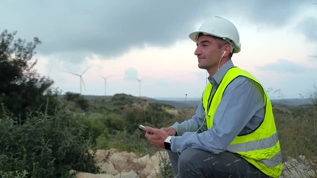 Employee of wind power listening to music on headphones and enjoying the magnificent view