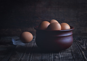 Chicken eggs in a clay bowl on a dark rustic table. Low key.
