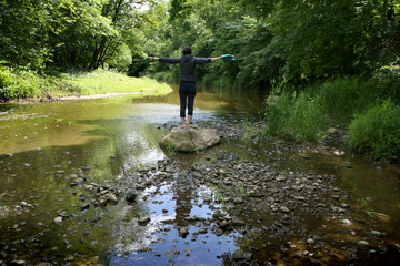 Woman in wild nature. Woman standing on stone in stream in summer.