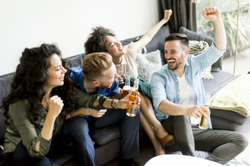 Friends watching TV , drinking cider and having fun in the room