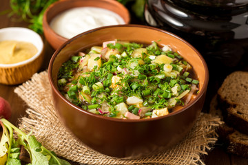 Okroshka. Traditional Russian summer cold soup with sausage, vegetables and kvass in bowl on wooden background.