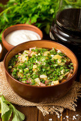 Okroshka. Traditional Russian summer cold soup with sausage, vegetables and kvass in bowl on wooden background.