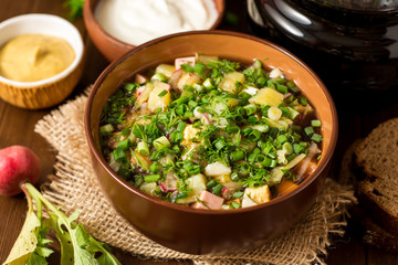 Okroshka. Traditional Russian summer cold soup with sausage, vegetables and kvass in bowl on wooden background.