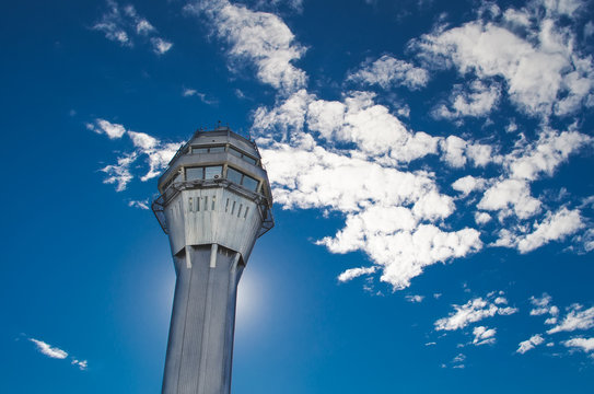 Airport traffic control tower with background of the sky and clouds.