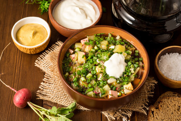 Okroshka. Traditional Russian summer cold soup with sausage, vegetables and kvass in bowl on wooden background.