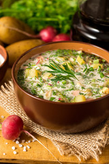 Okroshka. Traditional Russian summer cold soup with sausage, vegetables and kvass in bowl on wooden background.