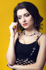 Obraz premium Portrait of a young beautiful dark haired concerned woman wearing black net top and glass beads looking worried and upset. Isolated on yellow background. Studio shot