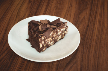 Delicious mosaic chocolate and biscuit cake served in white plate on wooden table