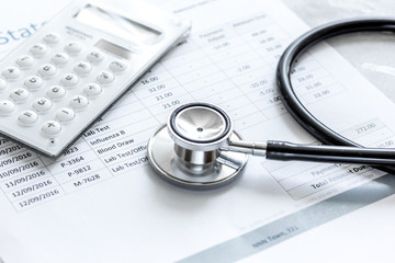 health care costs with billing statement, stethoscope and calculator on stone table