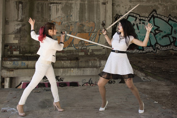 Two business women are fighting at swords. One of them is defeated
