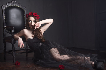 beautiful young woman with roses flower in hair, wearing black dress with make-up over dark background, gothic atmosphere. dark red lips.close-up fashion retouched portrait