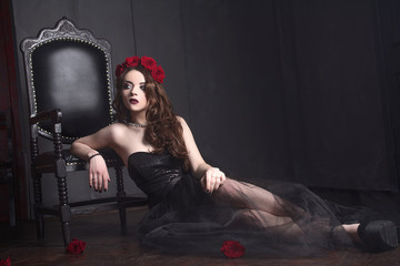 Obraz na płótnie Canvas beautiful young woman with roses flower in hair, wearing black dress with make-up over dark background, gothic atmosphere. dark red lips.close-up fashion retouched portrait
