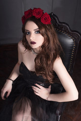 beautiful young woman with roses flower in hair, wearing black dress with make-up over dark background, gothic atmosphere. dark red lips.close-up fashion retouched portrait