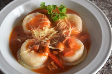 Upper view of a plate of sorrentinos - stuffed pasta - with sauce, parmesan cheese, and decorated with some parsley´s leaves