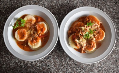 Upper detail view of two plates of sorrentinos - stuffed pasta - with sauce, parmesan cheese, and decorated with some parsley&acute;s leaves
