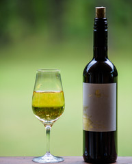 A glass with a white wine and the black wine bottle with label. Selective focus.