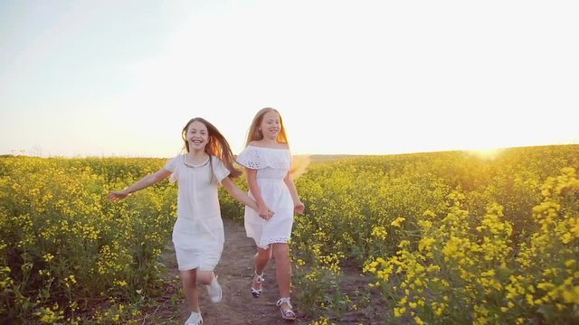 Two happy smiling girls running in the rape field with waving hair