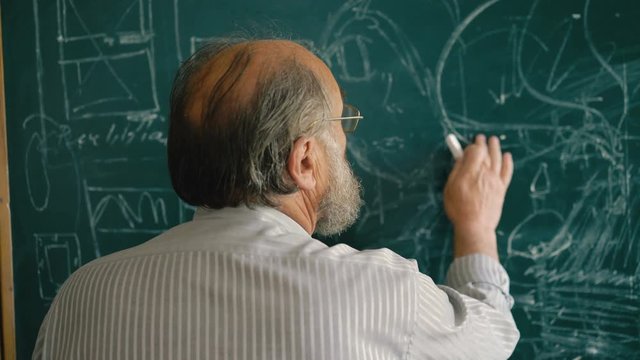Experienced old teacher explaining at the blackboard the schemes 4K