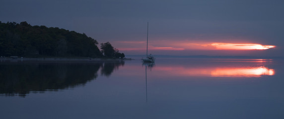 Sunrise over bay in northern Michigan with sailboat and foggy shore