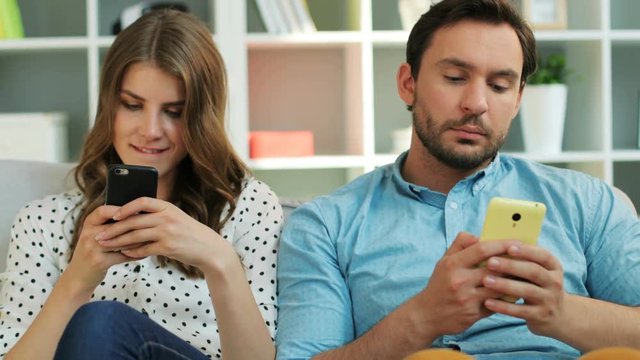 Young couple using cell phone while sitting on sofa at home in the living room.
