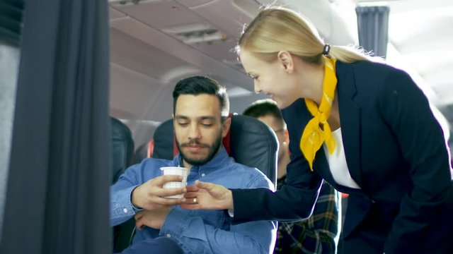 Airplane Stewardess/ Flight Attendant Brings Coffee for Handsome Hispanic Male Gentleman. They're Inflight. Business Class of a Commercial Aviation Interior is Visible. 4K UHD.