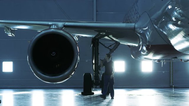 In a Hangar Aircraft Maintenance Engineer/ Technician/ Mechanic Visually Inspects Airplane's Jet Engine. Shot on RED EPIC-W 8K Helium Cinema Camera.
