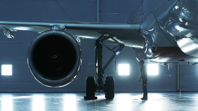 In a Hangar Aircraft Maintenance Engineer/ Technician/ Mechanic Inspects with a Flashlight Airplane's Jet Engine. Shot on RED EPIC-W 8K Helium Cinema Camera.