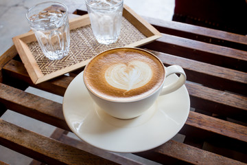Cup of latte or cappuccino with a glass of water on the table in cafe