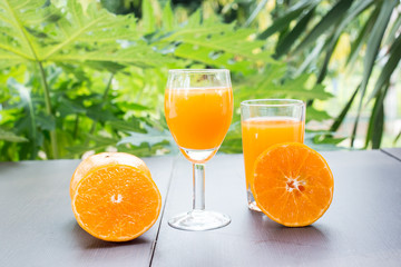 Close up of a glass of orange juice with cut and whole oranges on wooden table