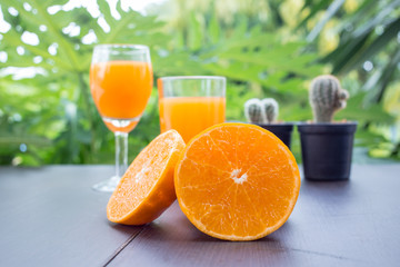 Close up of orange juice with cut and whole oranges on wooden table.