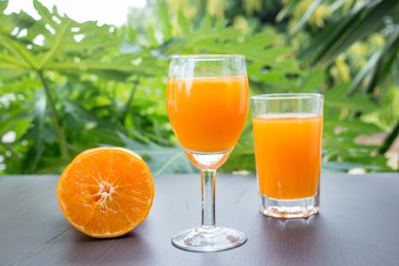 Close up of orange juice with cut and whole oranges on wooden table.