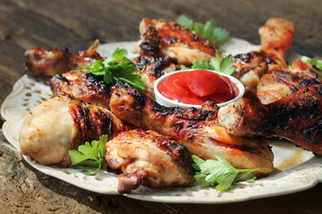 Grilled chicken legs on wooden table served on white plate with coriander