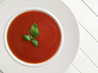 Tomato soup with basil herbs on white background. Top view.