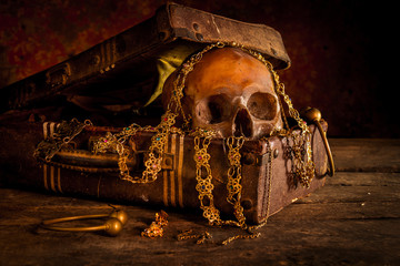 Still life with human skull with old treasure chest and gold, diamond and jewelry on wooden background
