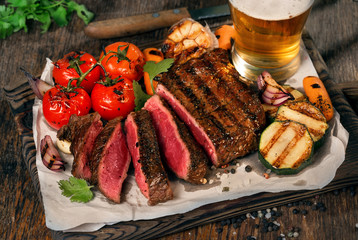 Sliced rare grilled steak with grilled vegetables and lager beer