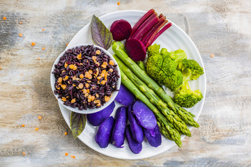 Delicious and healthy colorful vegetables with black rice and lentils on wooden table in the garden. Rainbow food and balanced food. 
