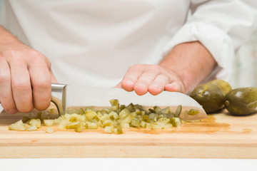 Chef's hands with knife cutting the pickled cucumber on the wooden board. Preparation for cooking. Healthy eating and lifestyle.
