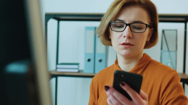 Young business woman in glasses talking on smart phone and checking the final report for the month in the office background.