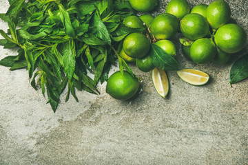 Flatlay of freshly picked organic limes and mint for making cocktail or lemonade over grey concrete stone background, top view, copy space
