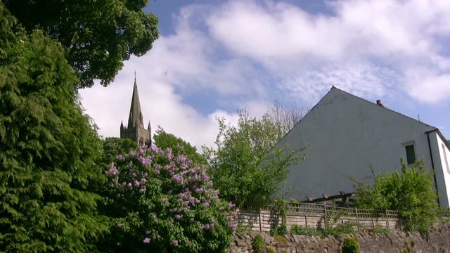 The small market town town of Alston, Cumbria, England with a white cottage and the church spire framed by trees and white summer clouds scudding by.