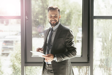 Fototapeta premium smiling businessman in suit using digital tablet at modern office