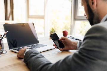 side view of businessman using smartphone while working on laptop at workplace