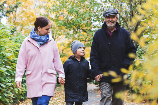 Happy senior man walking with great grandson and daughter in park during autumn