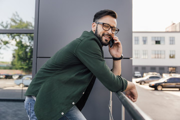 smiling bearded young man in eyeglasses using smartphone