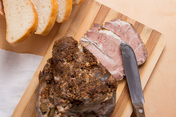 Baked pork with herbs and spice on wooden board and and slices white wheat bread.