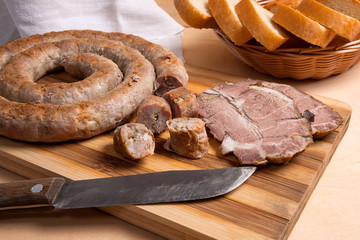 Sliced roasted traditional homemade sausage with spices and herbs. Baked pork with herbs and spice on wooden board and and slices white wheat bread.
