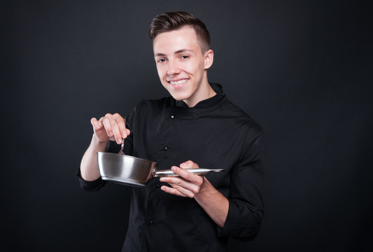 Joyful young cook stirring with spoon in saucepan
