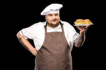 cooker holding burgers on plate and looking at camera isolated on black