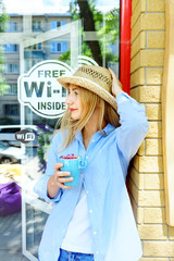 Pretty and young girl in straw hat and jeans wear holding a cup of aroma cappuccino. Teenage thinking and happy looking
