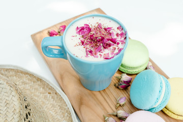 Fototapeta na wymiar Closeup view on straw hat and blue cup of aroma cappuccino with french tasty macarons